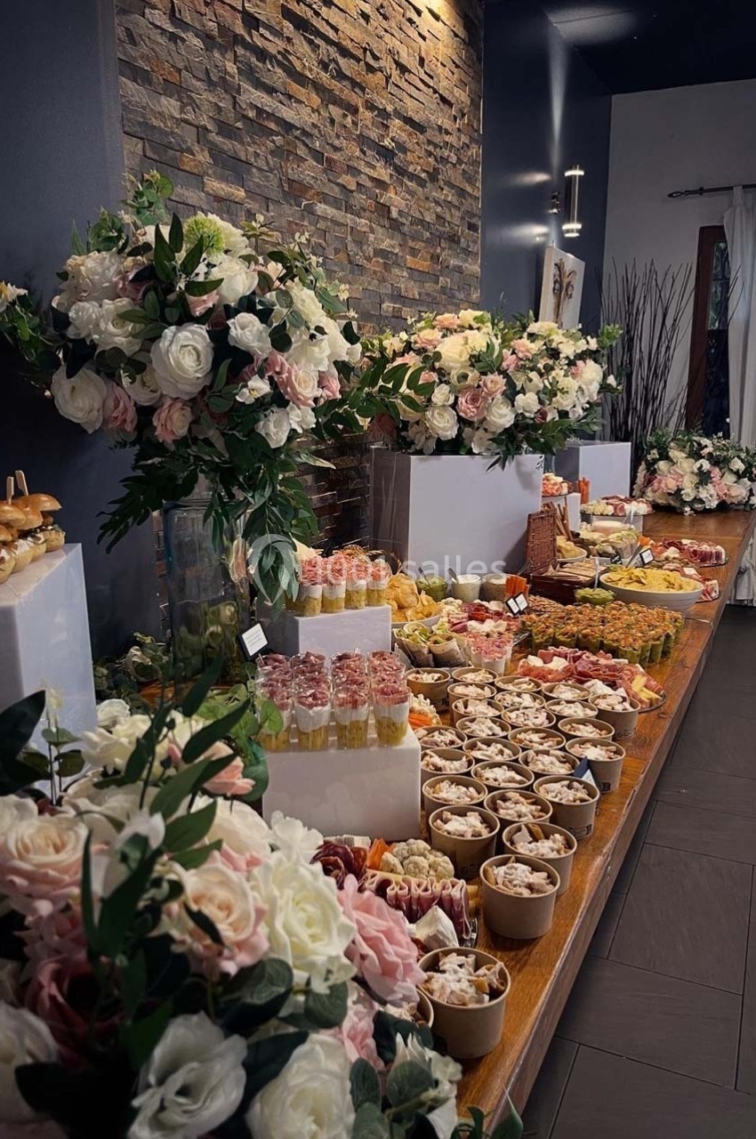 Buffet varié avec fleurs décoratives, comprenant amuse-bouches, desserts et boissons, présenté sur une longue table.