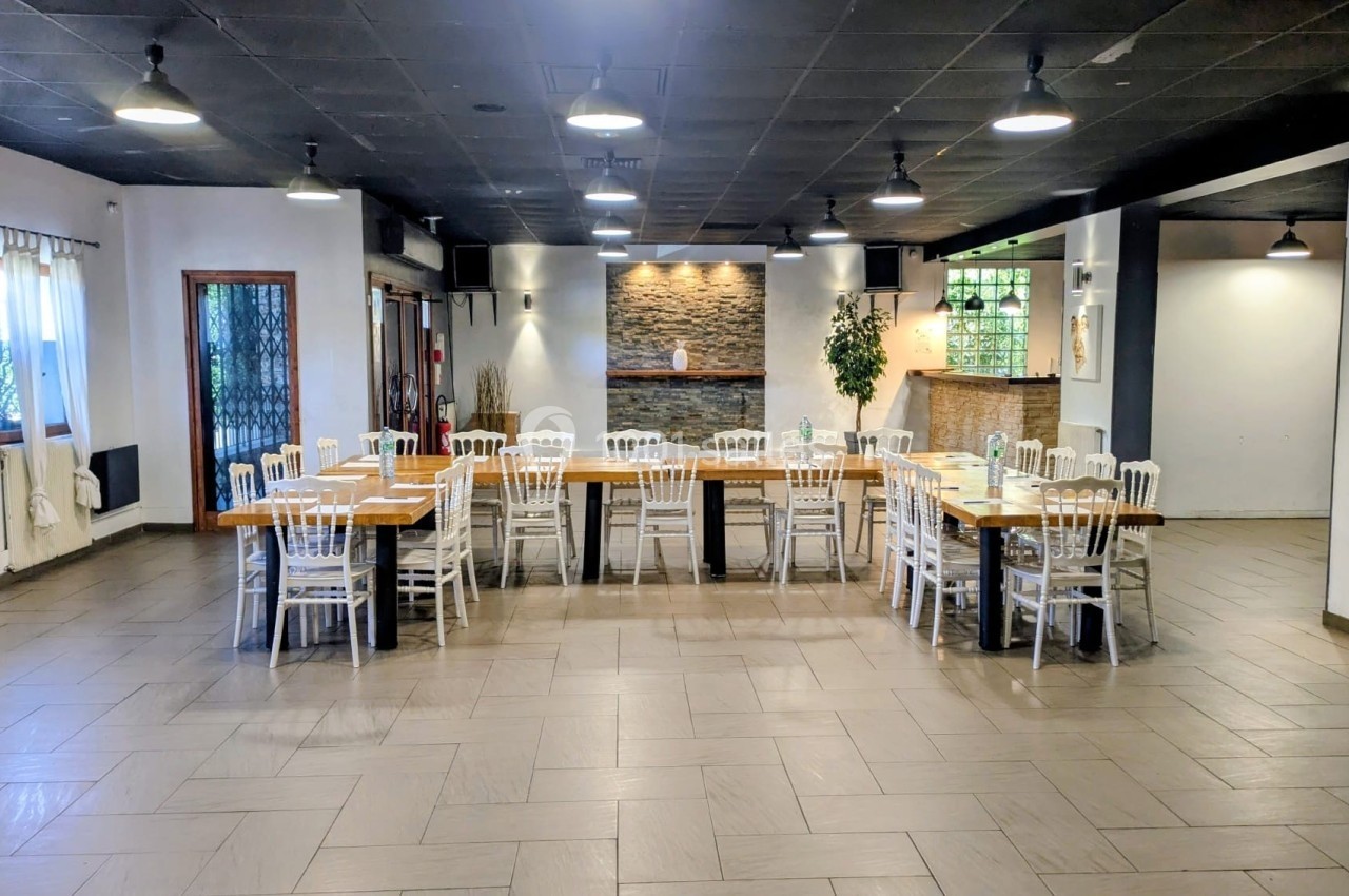 Salle lumineuse avec tables en bois disposées en U, chaises blanches, murs clairs et éclairage suspendu.