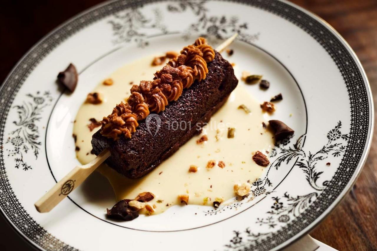 Dessert au chocolat sur bâtonnet, nappé de crème anglaise et garni de noisettes concassées sur une assiette décorée.