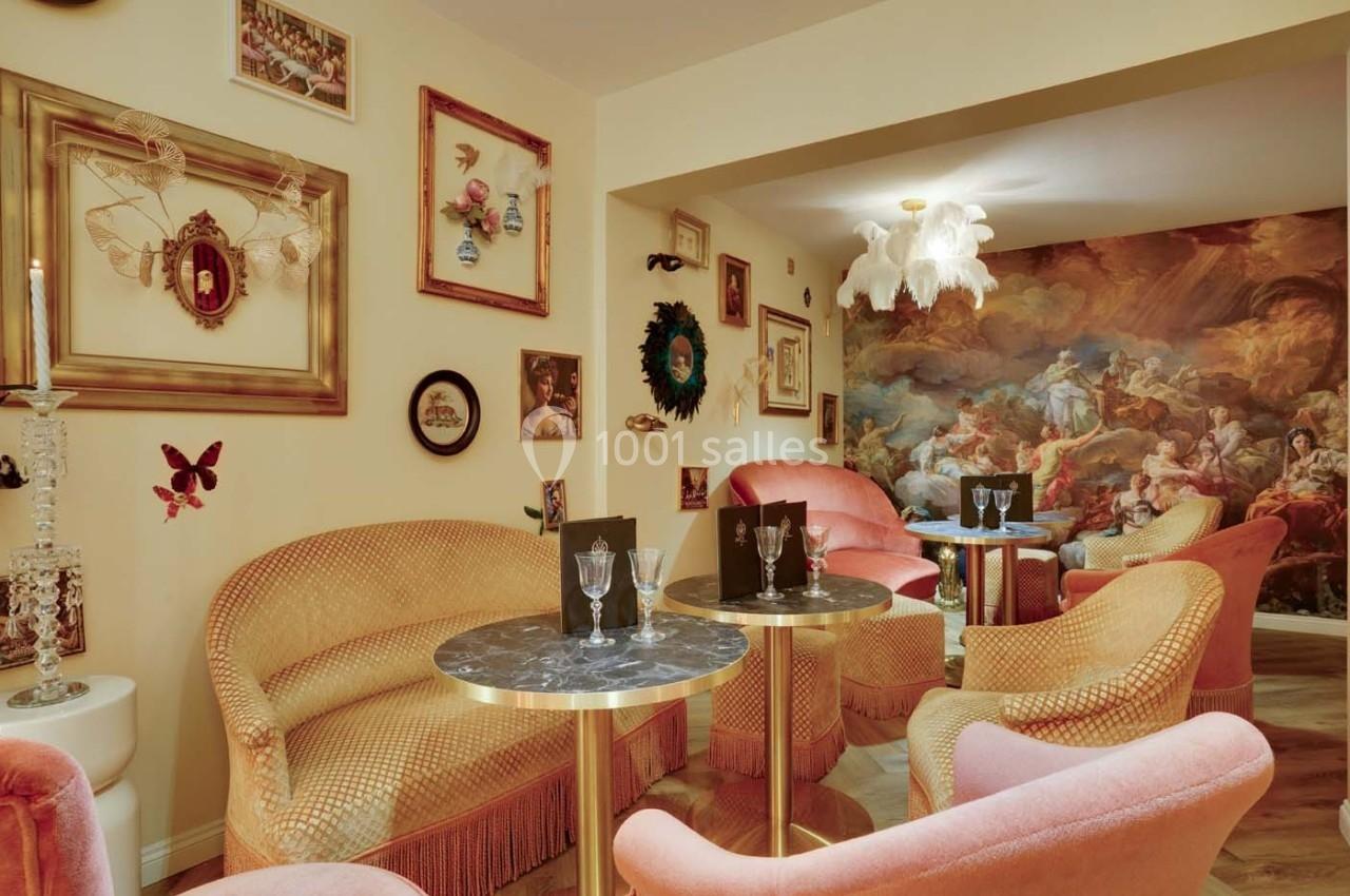 Salon cosy avec fauteuils pastel, tables en marbre, décorations murales éclectiques et fresque murale baroque.