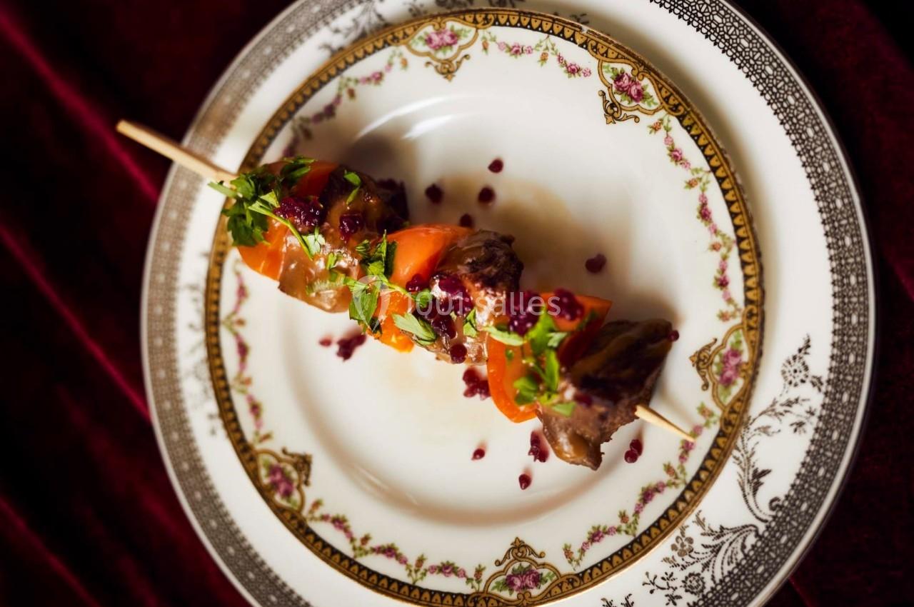 Brochette de viande et légumes garnie de persil et de sauce, servie sur une assiette décorative.