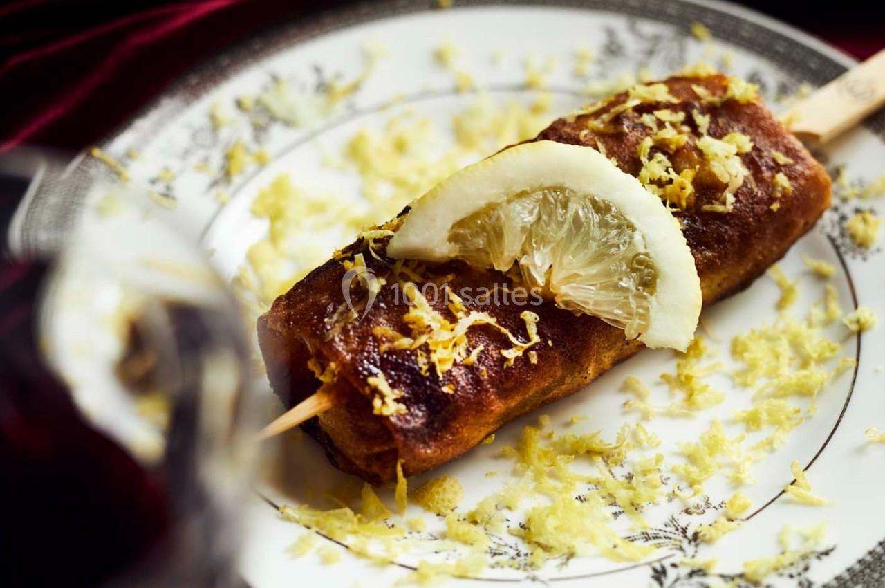 Brochette de dessert dorée garnie de zeste et tranche de citron, présentée sur une assiette décorative.