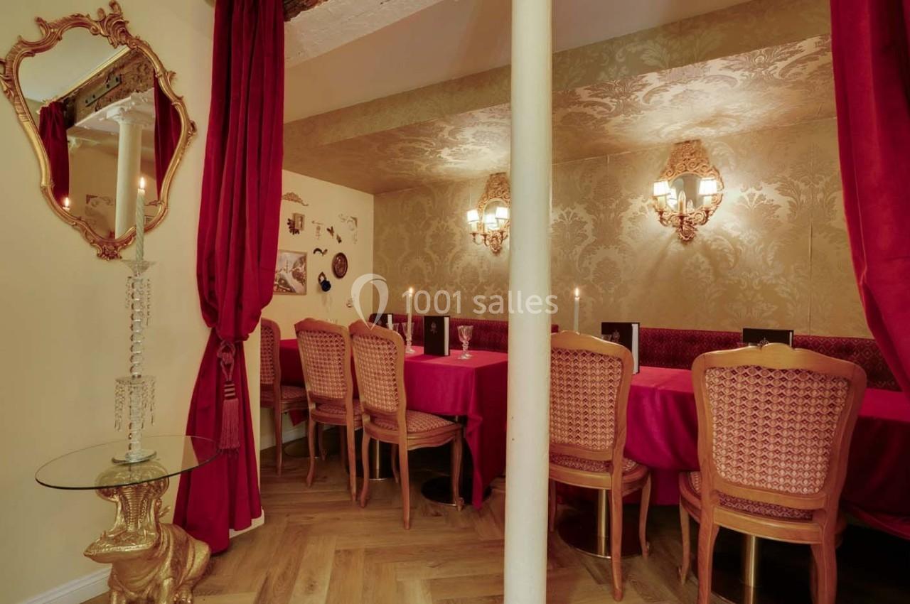 Salle à manger élégante avec table rouge, chaises en bois sculpté, murs ornés et éclairage tamisé.