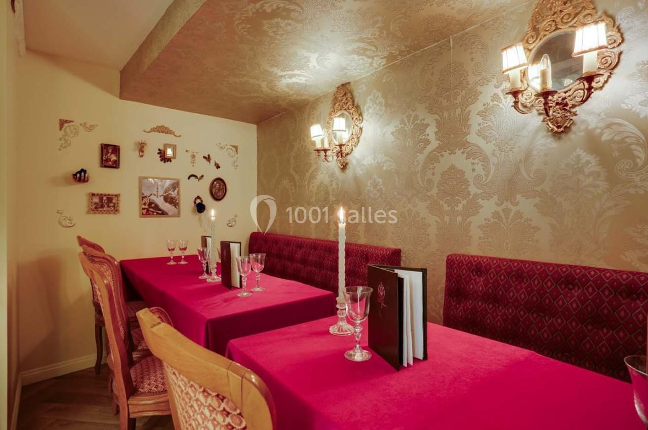 Salle à manger élégante avec murs ornés de motifs dorés, tables rouges dressées et éclairage chaleureux.