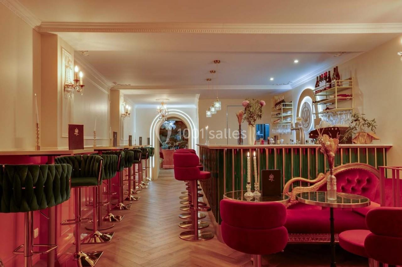 Intérieur d'un bar élégant avec comptoir coloré, tabourets verts, fauteuils rouges et éclairage chaleureux.