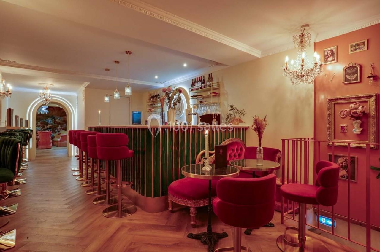 Intérieur d'un bar élégant avec des fauteuils rouges, un comptoir vert, un éclairage chaleureux et une décoration raffinée.