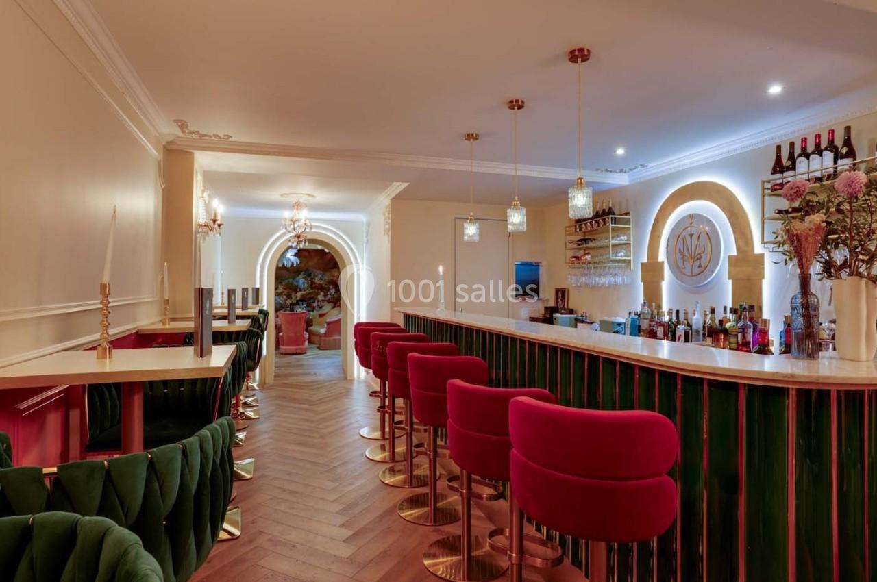 Intérieur d'un bar élégant avec comptoir vert, tabourets rouges, éclairage chaleureux et décoration raffinée.
