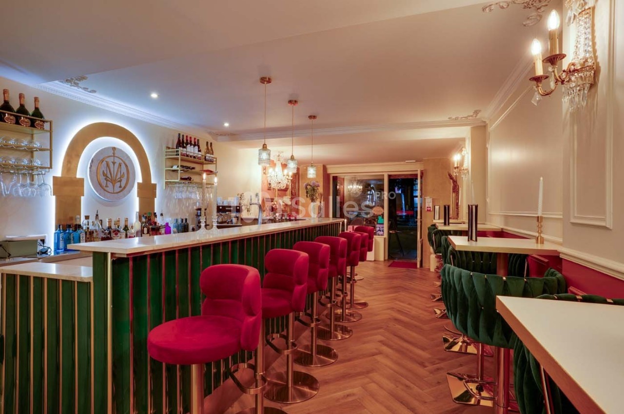 Intérieur d'un bar élégant avec comptoir central, tabourets rouges, parquet en bois et éclairage chaleureux.