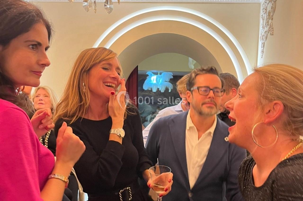 Des personnes discutent et rient dans une pièce éclairée, avec un décor intérieur élégant en arrière-plan.