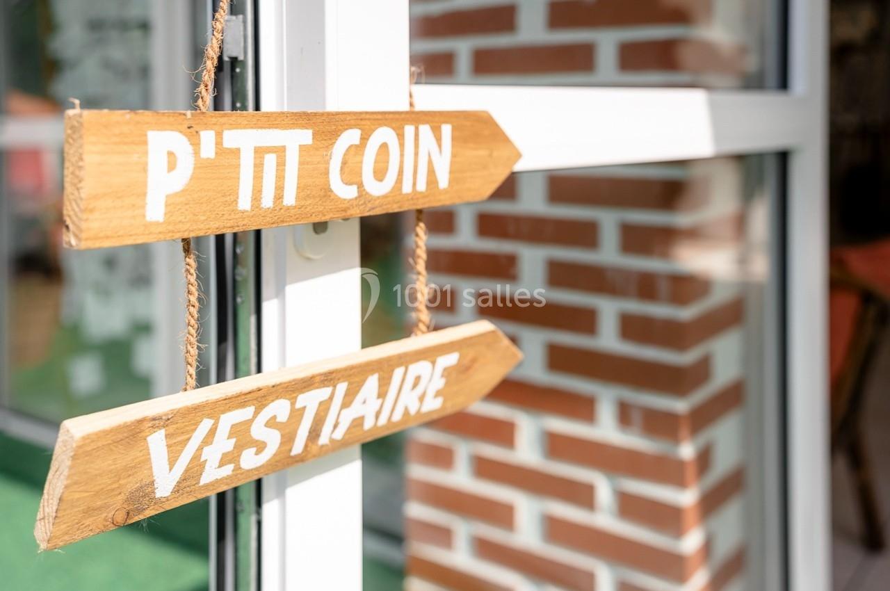Deux panneaux en bois indiquant ’P'tit coin’ et ’Vestiaire’ accrochés près d'une porte vitrée.