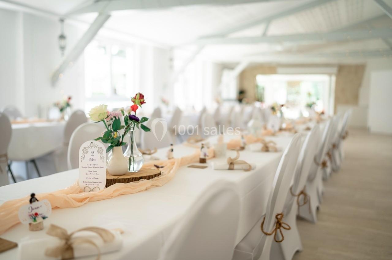 Salle lumineuse décorée pour un événement, avec des tables blanches ornées de fleurs et de nappes pastel.