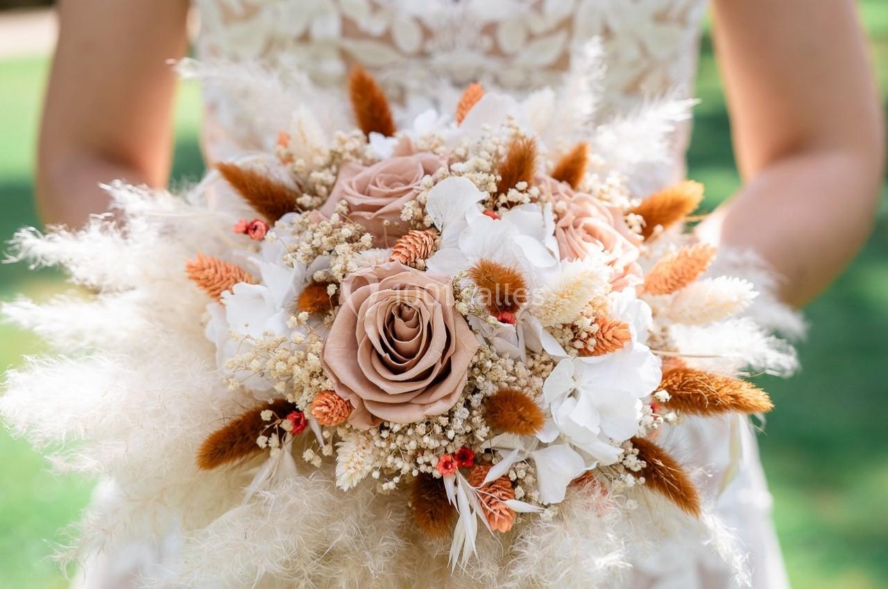 Bouquet de fleurs séchées et fraîches avec des roses beige, des épis et des pampas, tenu par une personne en robe blanche.
