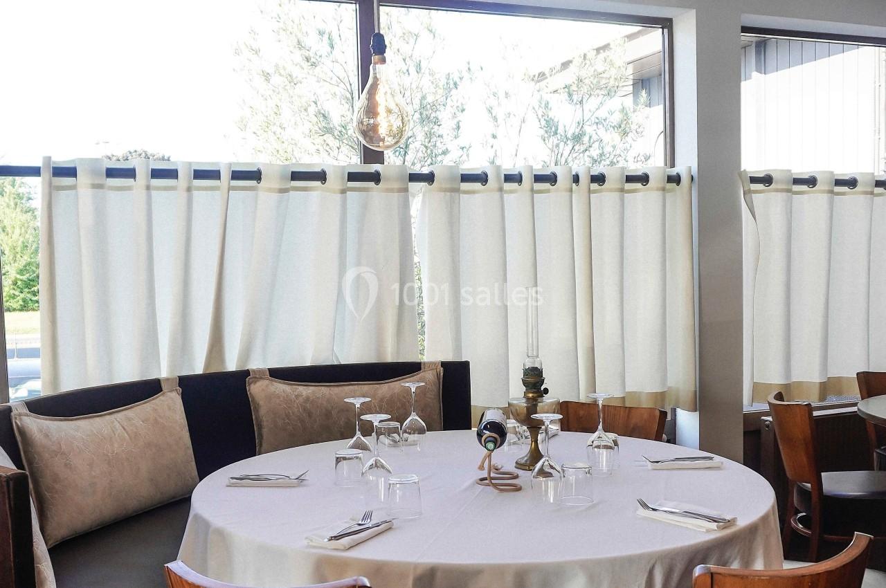 Table ronde dressée avec nappes blanches, verres et couverts, entourée de chaises en bois dans un restaurant lumineux.
