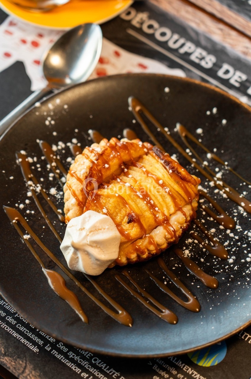 Tartelette aux pommes caramélisées avec une touche de chantilly, servie sur une assiette décorée de filet de caramel.