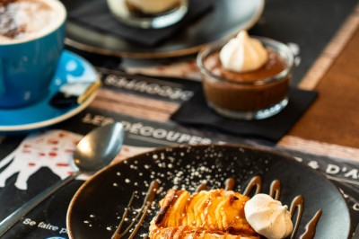 Desserts variés sur une table, incluant un tiramisu décoré d'une tranche d'orange, une mousse au chocolat et un cappuccino.