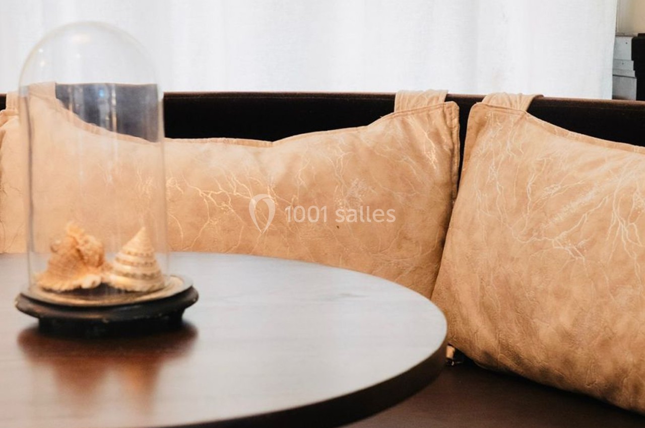 Coussins beiges texturés disposés sur une banquette en bois sombre, avec une cloche en verre contenant des coquillages.