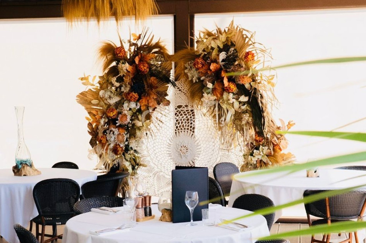Décoration florale bohème avec des tons chauds et naturels, entourée de tables dressées dans une salle lumineuse.