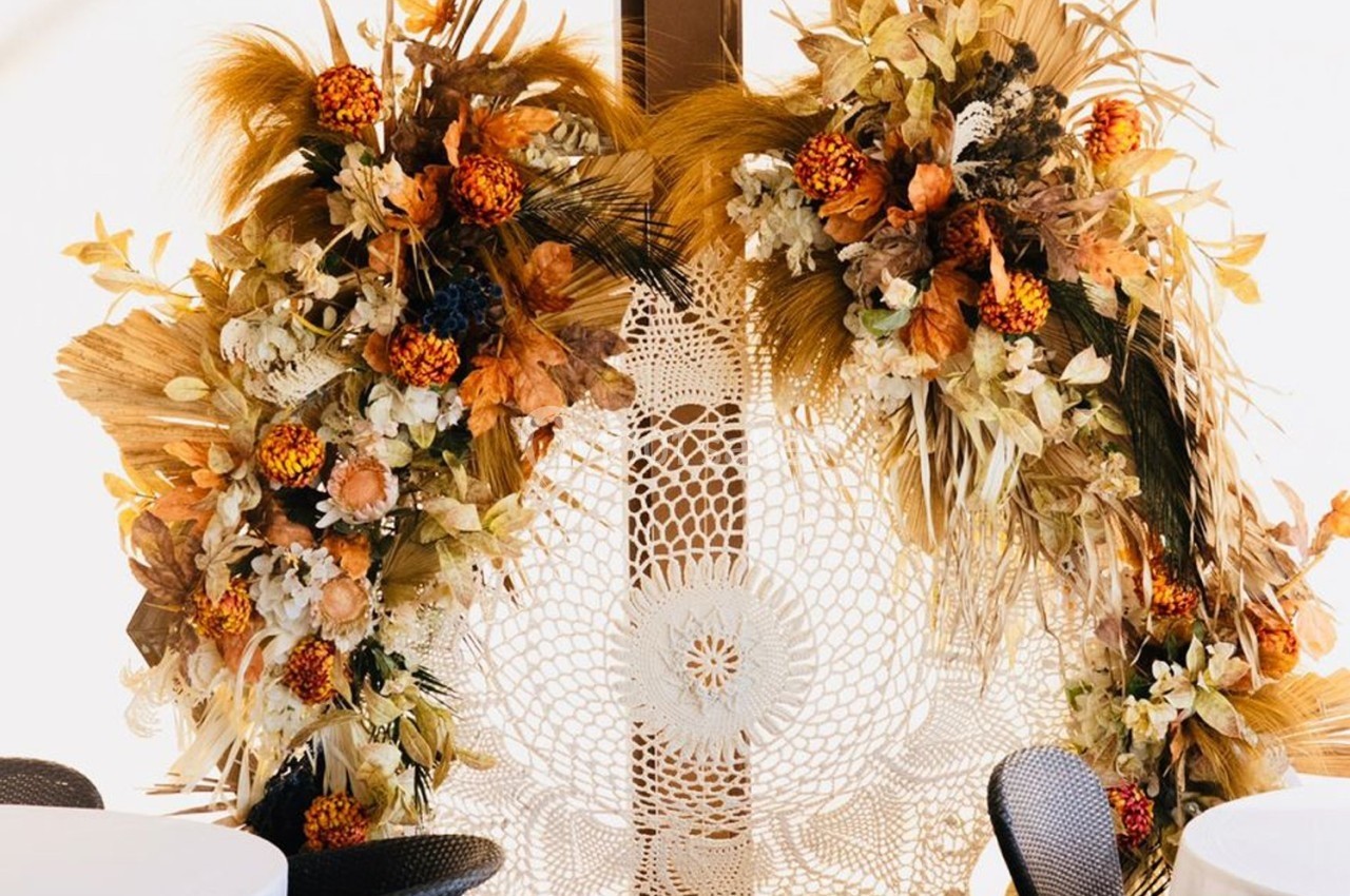 Décoration florale automnale avec des fleurs séchées et des feuillages entourant un napperon en dentelle blanche.