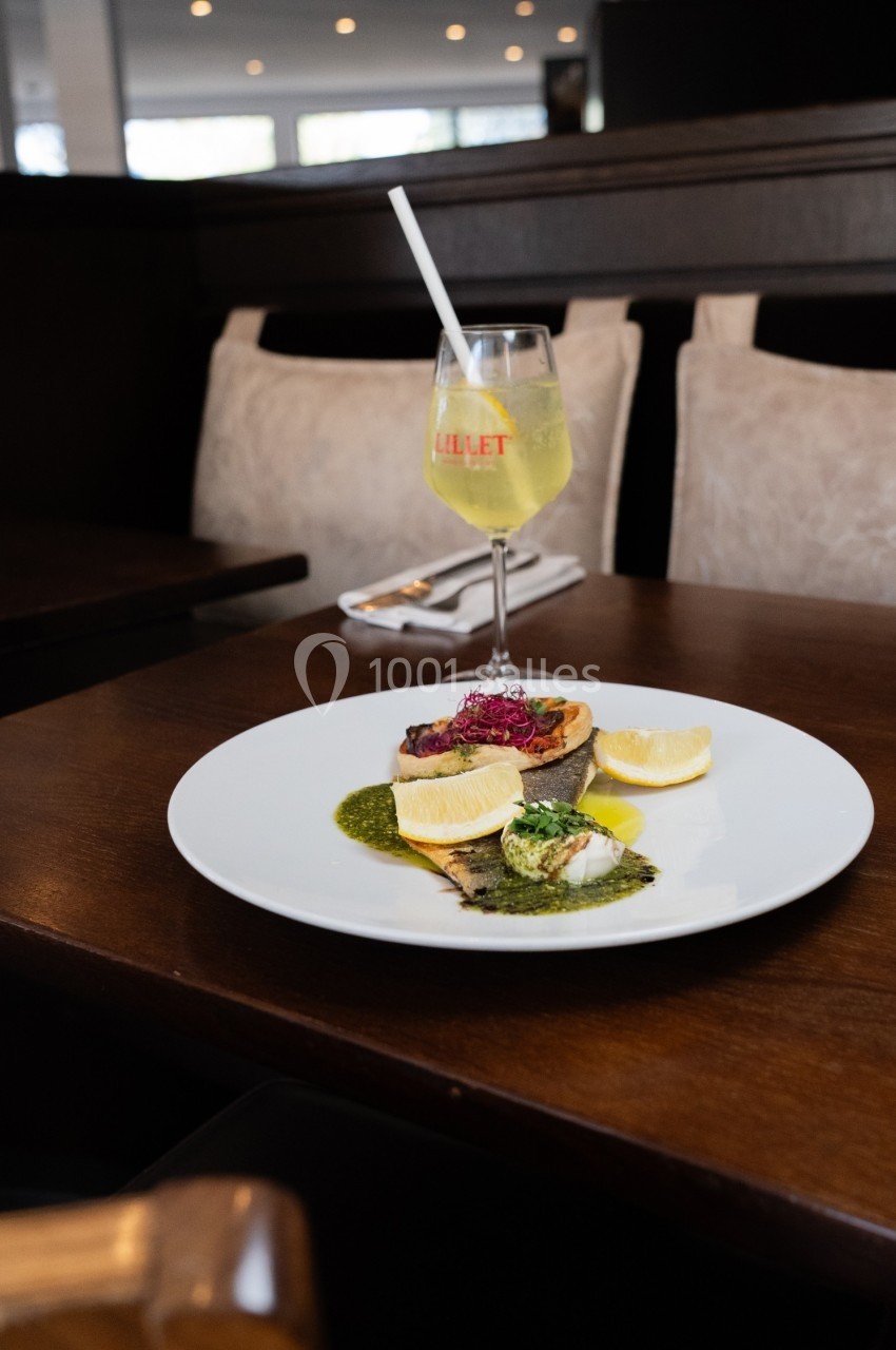 Assiette de saumon grillé avec sauce verte, citron et garniture, accompagnée d'un verre de cocktail sur une table.