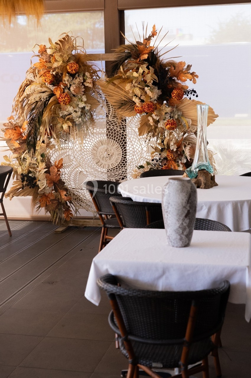 Décoration florale automnale avec des tons orange et beige, placée près de tables dressées dans un espace intérieur lumineux.