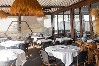 Plantes vertes en pot décorant une terrasse couverte avec des tables et des chaises disposées en arrière-plan.