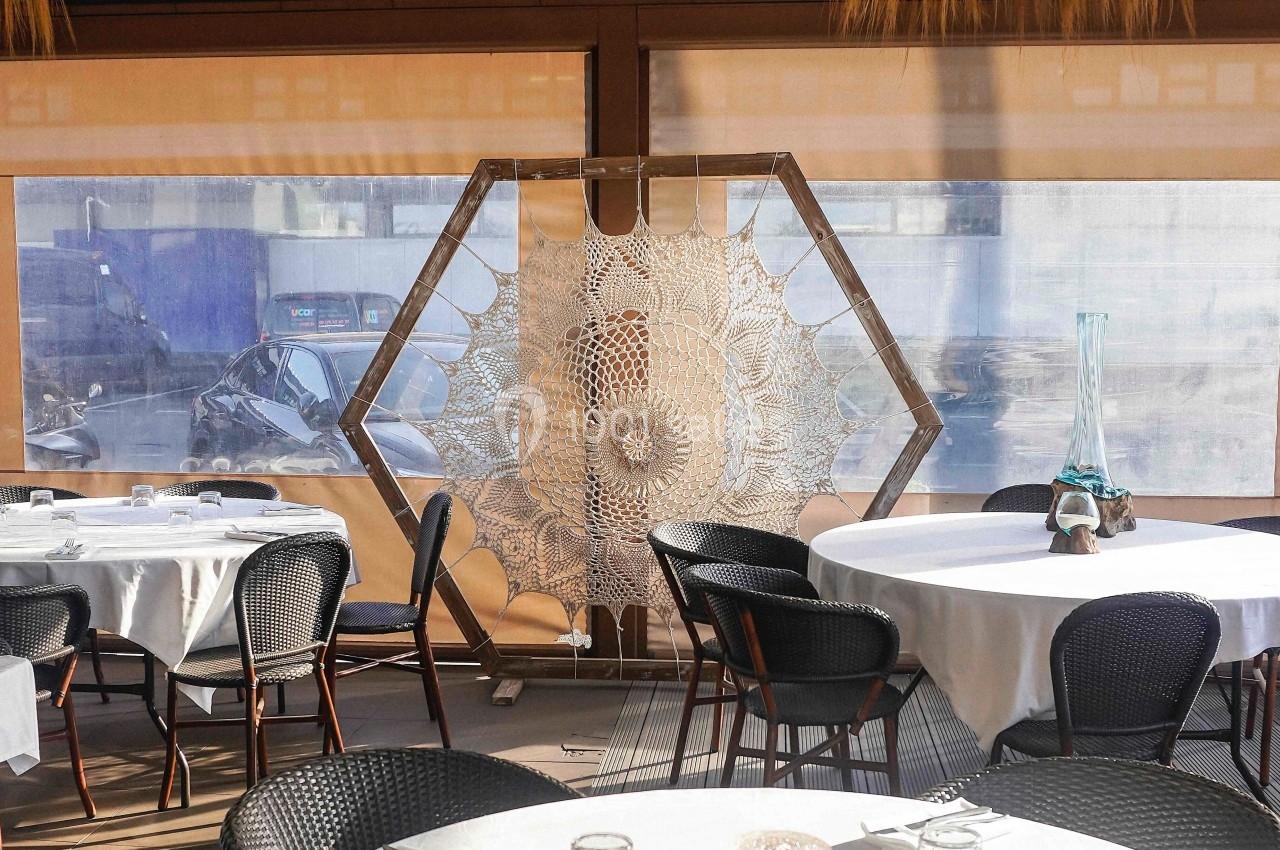 Décoration en macramé hexagonale suspendue dans un restaurant avec des tables dressées et des chaises noires.