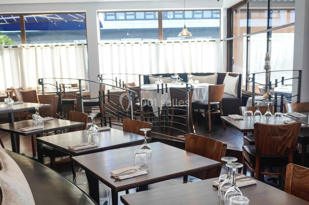 Salle de restaurant lumineuse avec des tables en bois dressées, des chaises assorties et de grandes fenêtres.