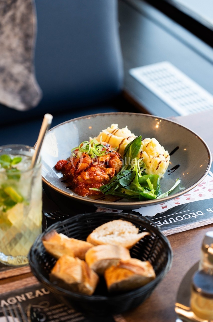 Assiette contenant du poulet en sauce, purée, légumes verts, accompagnée de pain et d'une boisson fraîche.