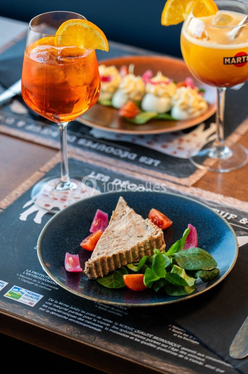 Assiette de terrine avec salade et tomates, accompagnée de cocktails garnis d'une tranche d'orange sur une table.