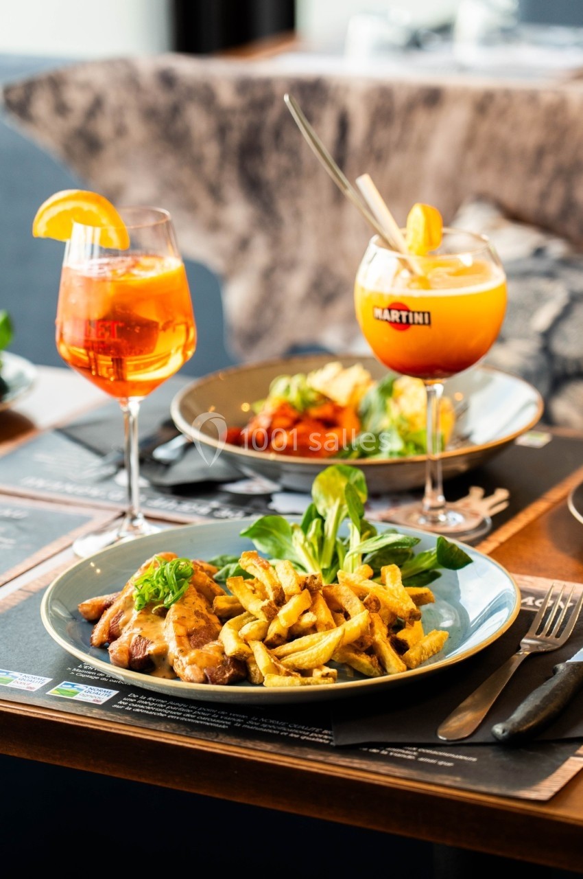 Assiette de viande avec frites et salade, accompagnée de cocktails colorés sur une table de restaurant.