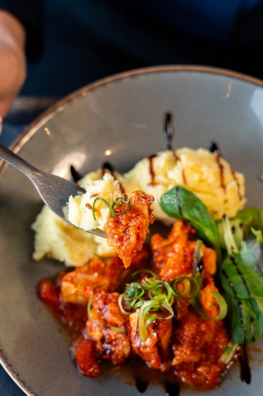 Assiette contenant de la purée de pommes de terre, du poulet en sauce rouge et des légumes verts, avec une fourchette en…