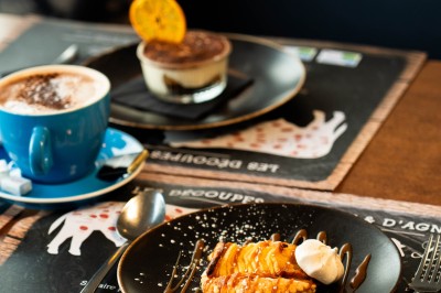 Dessert tiramisu dans une verrine, décoré d'une tranche d'orange séchée, avec une main tenant une cuillère.