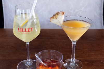 Trois cocktails variés sur une table en bois, comprenant un verre de Lillet, un cocktail au martini et un verre de Negroni.