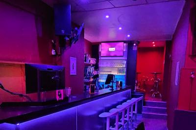 Écran et panneau indiquant ’Karaoké Bar Sablon’ avec un micro, dans une salle éclairée par des lumières violettes.