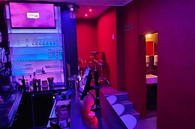 Écran et panneau indiquant ’Karaoké Bar Sablon’ avec un micro, dans une salle éclairée par des lumières violettes.