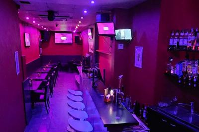 Écran et panneau indiquant ’Karaoké Bar Sablon’ avec un micro, dans une salle éclairée par des lumières violettes.