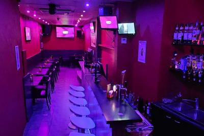 Miniature Location salle Bruxelles (Bruxelles-Capitale) - Karaoke Bar Sablon #5 Scène de karaoké dans un bar avec éclairage rose et rouge, micro illustré sur un panneau mural.