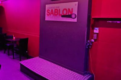 Miniature Location salle Bruxelles (Bruxelles-Capitale) - Karaoke Bar Sablon #7 Scène de karaoké dans un bar avec éclairage rose et rouge, micro illustré sur un panneau mural.