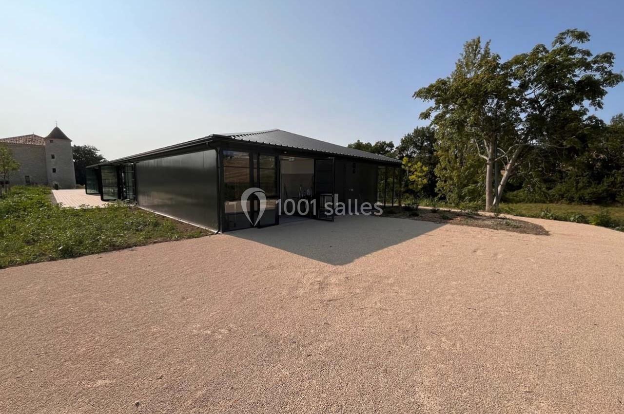 Bâtiment moderne avec façade vitrée, entouré de végétation et d'une allée en gravier sous un ciel dégagé.