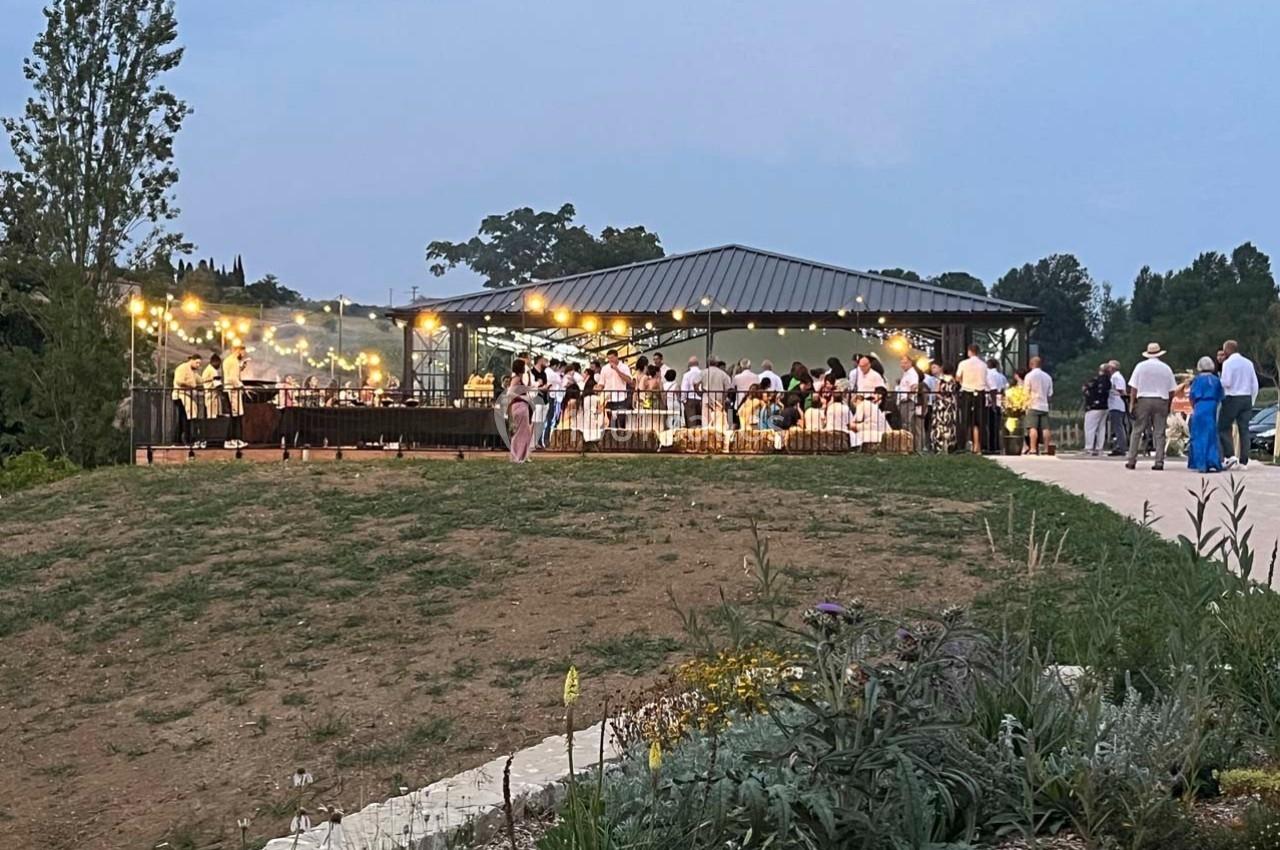 Groupe de personnes rassemblées sous un pavillon éclairé par des guirlandes lumineuses dans un cadre extérieur verdoyant.