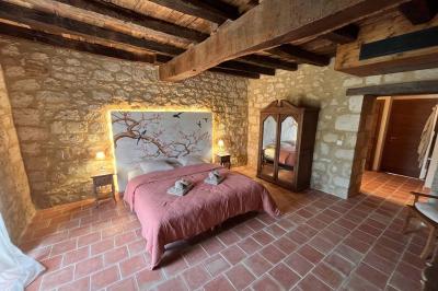 Chambre avec lit double, murs en pierre, poutres apparentes et éclairage doux, décorée de motifs muraux naturels.