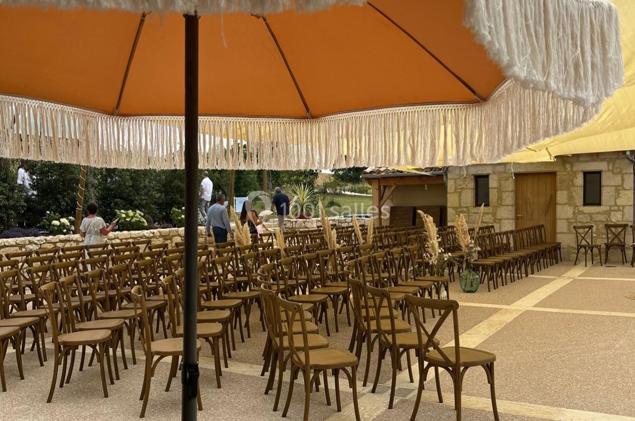 Chaises en bois disposées sous des parasols orange sur une terrasse en plein air, avec quelques personnes en arrière-plan.