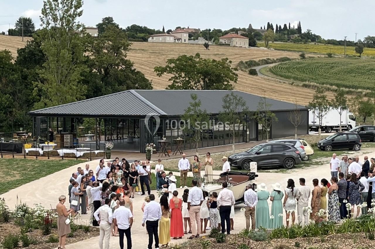 Groupe de personnes rassemblées en extérieur près d'un bâtiment moderne, entouré de champs et de végétation.