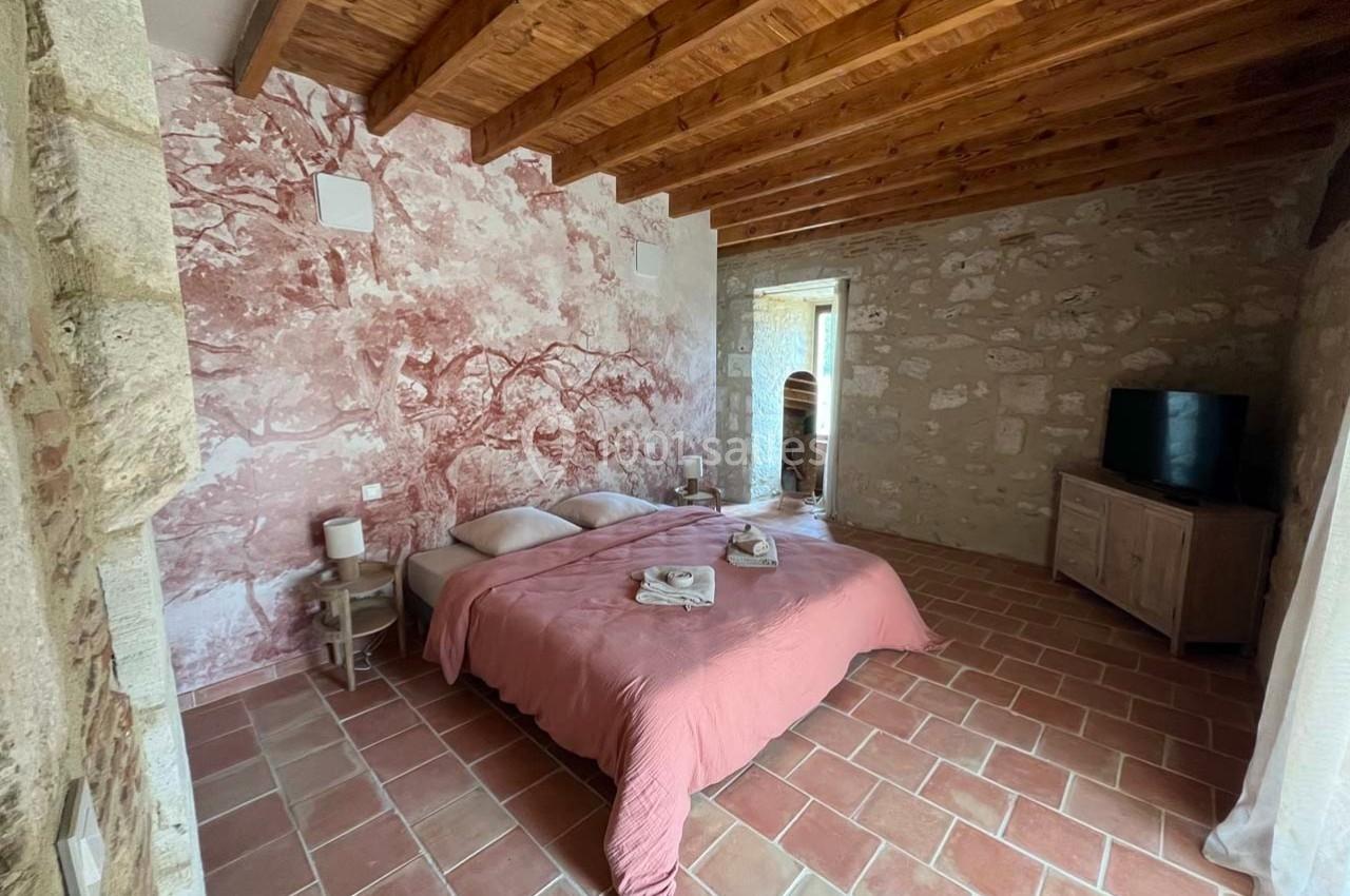 Chambre avec murs en pierre, plafond en bois, lit double avec couverture rose et sol en carrelage.