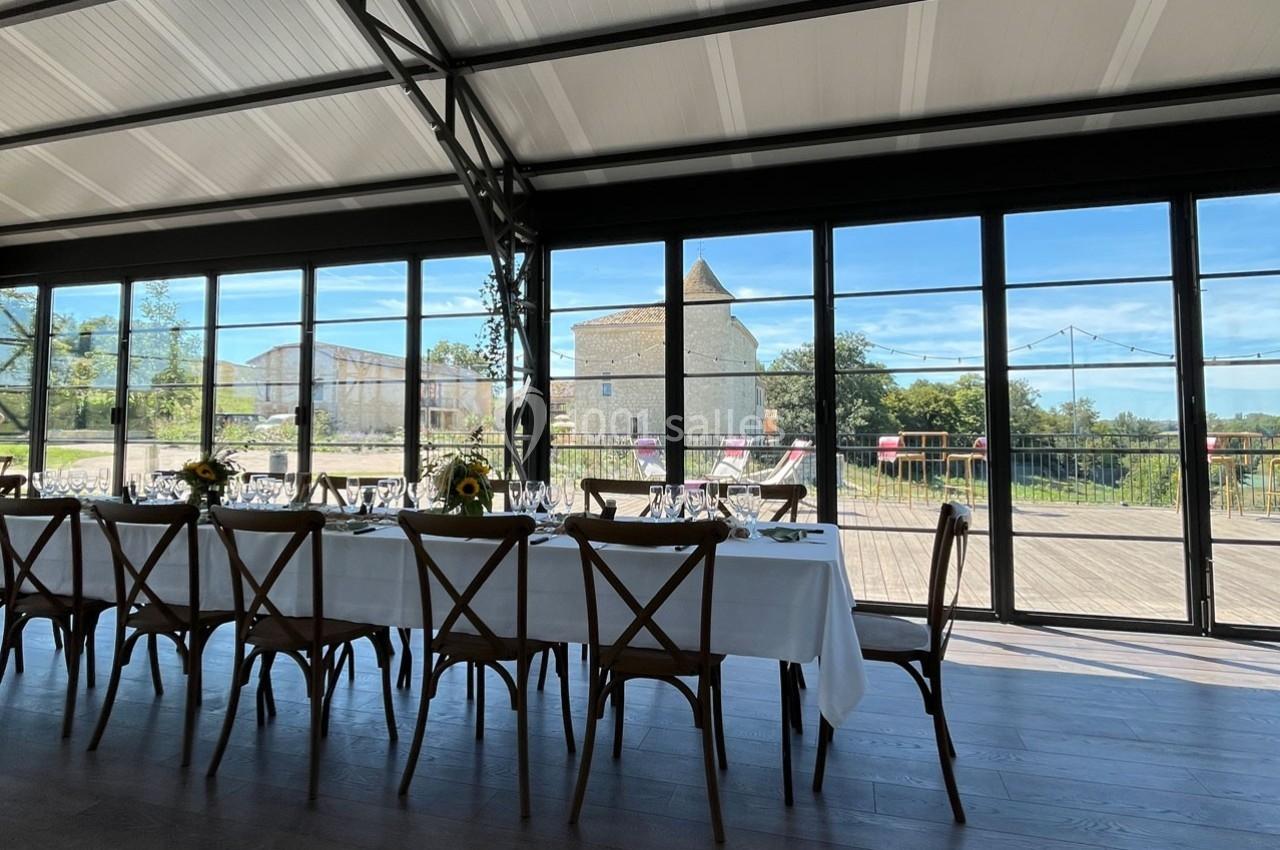 Salle lumineuse avec grande baie vitrée donnant sur une terrasse et un paysage rural avec une tour en pierre.