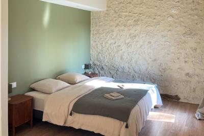 Chambre lumineuse avec un lit double, mur jaune, parquet en bois, escalier et coin détente avec fauteuils pliants.