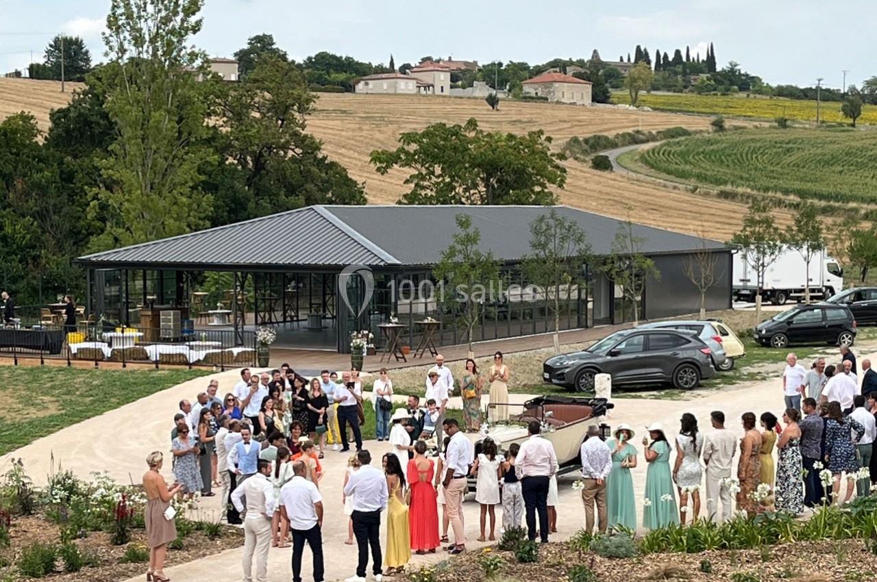 Groupe de personnes rassemblées en extérieur près d'un bâtiment moderne, entouré de champs et de végétation.