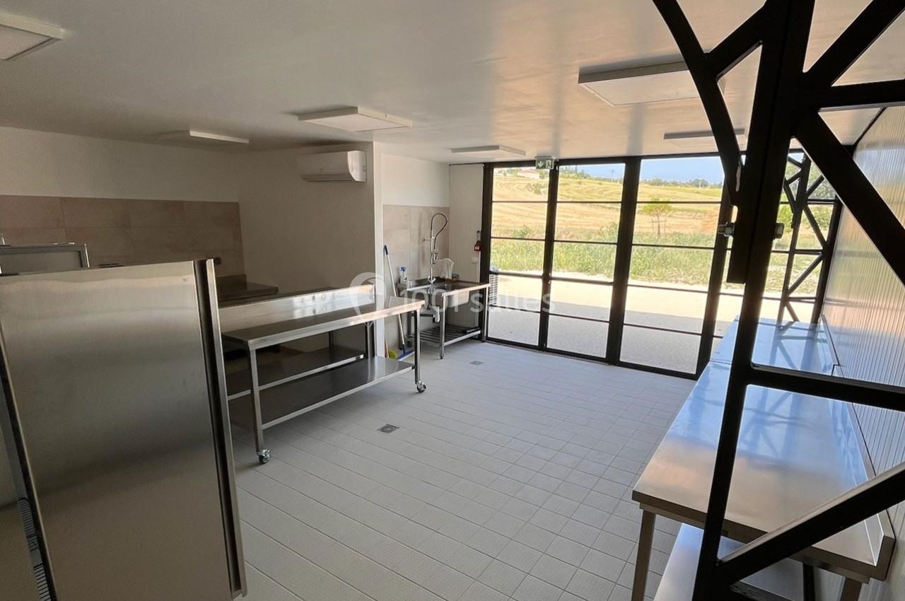 Cuisine professionnelle lumineuse avec plans de travail en inox, sol carrelé clair et grande baie vitrée donnant sur l…