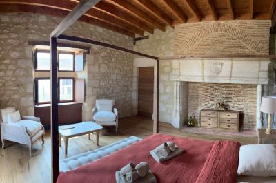 Chambre lumineuse avec un lit double, mur jaune, parquet en bois, escalier et coin détente avec fauteuils pliants.