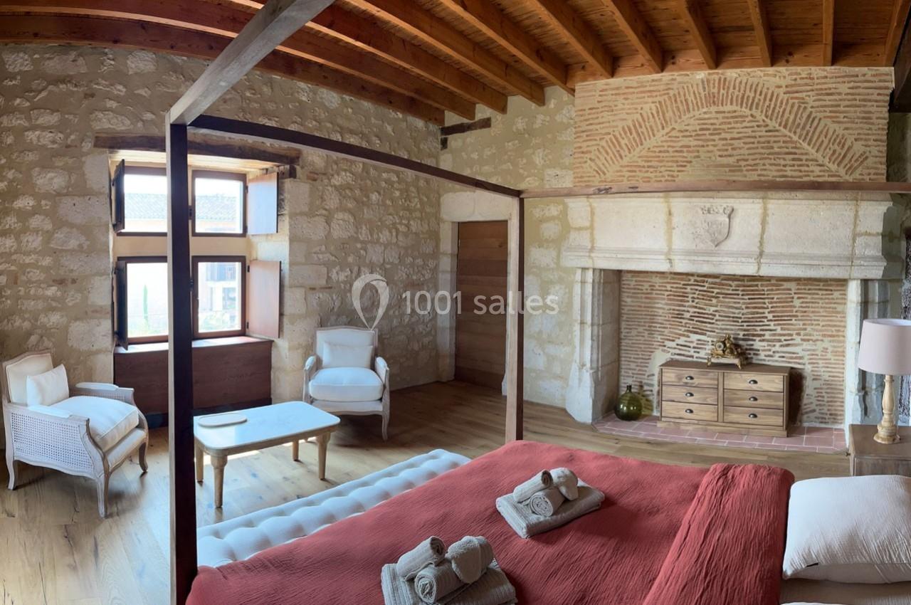 Chambre avec lit à baldaquin, cheminée en pierre, plafond en bois et mobilier élégant dans un décor rustique.